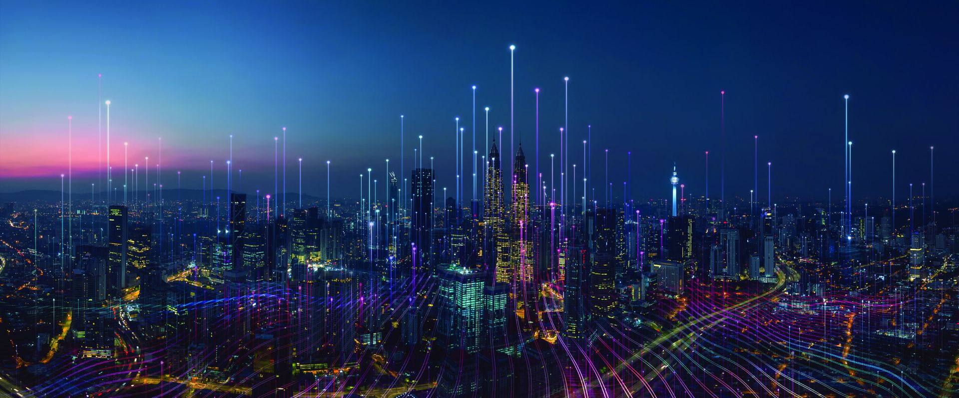 A vibrant city skyline at dusk, featuring tall skyscrapers illuminated with colorful lights. Radiating beams of light in various colors extend upward into the sky, creating a dynamic and modern visual effect.