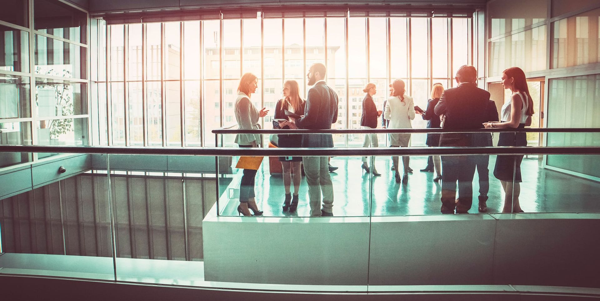 A group of professionals engage in conversation in a modern office space with large glass windows, illuminating the area with natural light.