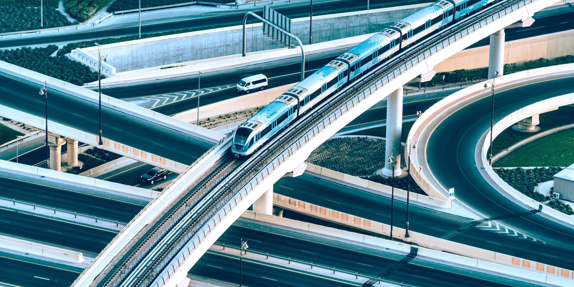 A modern train travels along an elevated track above a complex network of highways and overpasses, showcasing a blend of transportation infrastructure.