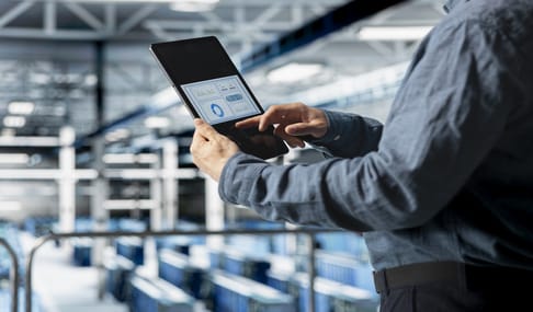 A person in a blue shirt is using a tablet to interact with a digital interface displaying data, standing in a modern industrial setting.