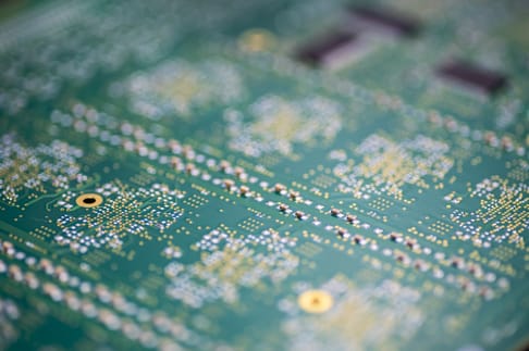 Close-up of a green printed circuit board with intricate patterns of copper traces and soldered connections.