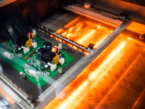 Zwei Leiterplatten in einem Ofen, umgeben von orangefarbenem Licht und Heat-Shields.