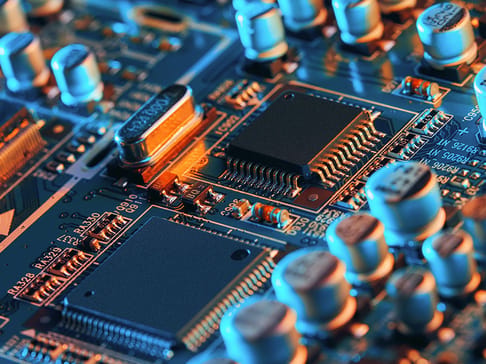 Close-up of a detailed circuit board featuring various electronic components, including microchips and capacitors, illuminated with blue and orange lighting.