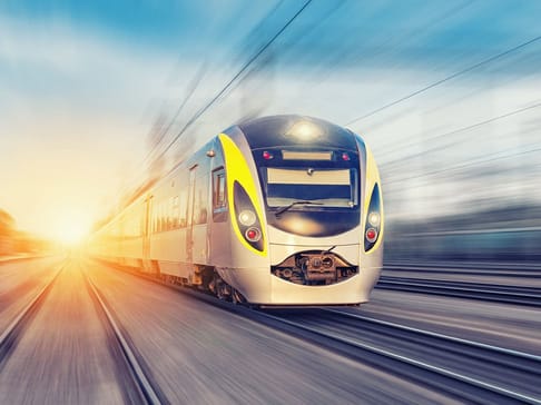速いスピードで走る電車が、朝日を背景に線路を進んでいる。
