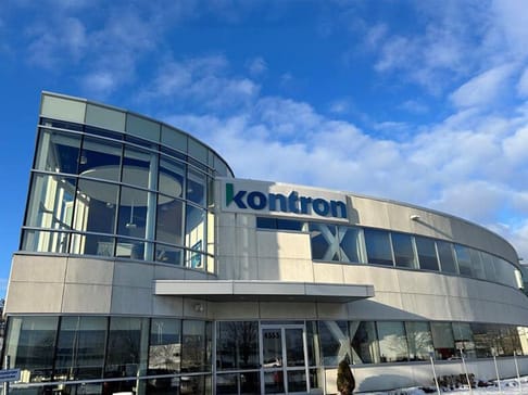 Modern building exterior featuring large glass windows and the name "kontron" prominently displayed on the facade. The sky is partly cloudy.