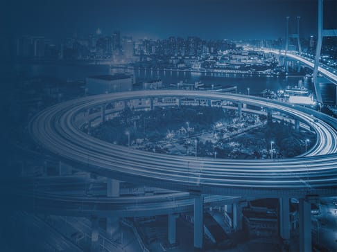 Eine nächtliche Stadtansicht mit einer interaktiven Autobahn, die in einem kreisförmigen Muster verläuft. Hochhäuser glitzern im Hintergrund vor einer tiefblauen Skyline, während Lichter auf der Straße sichtbar sind.