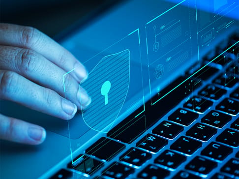 A hand interacts with a holographic security shield displayed above a laptop keyboard, emphasizing digital security technology.