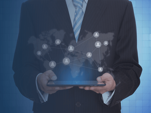 A businessman in a suit holds a tablet, with a transparent world map and connected user icons overlaying the image, symbolizing global networking and technology.